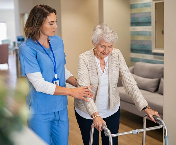 Young nurse helping senior patient using a walking frame to walk in hospital corridor